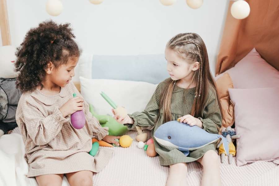Deux petites filles assises sur un lit en train de partager ses jouets en bois.