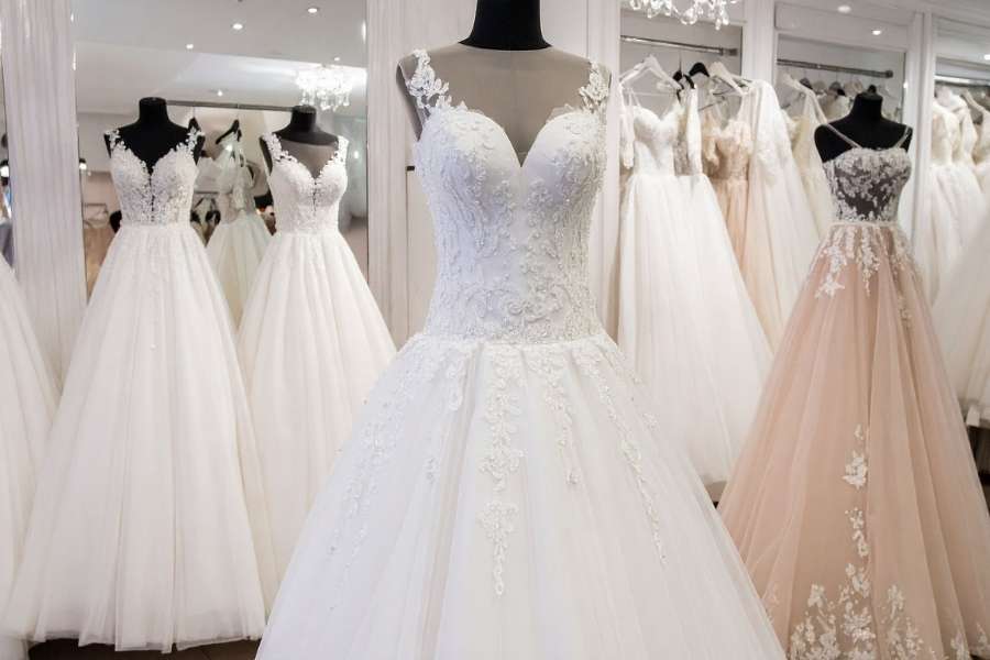 Une sélection de plusieurs robes de mariée blanches et ornées sur des mannequins dans une boutique élégante, avec une robe de mariée parfaite au premier plan.