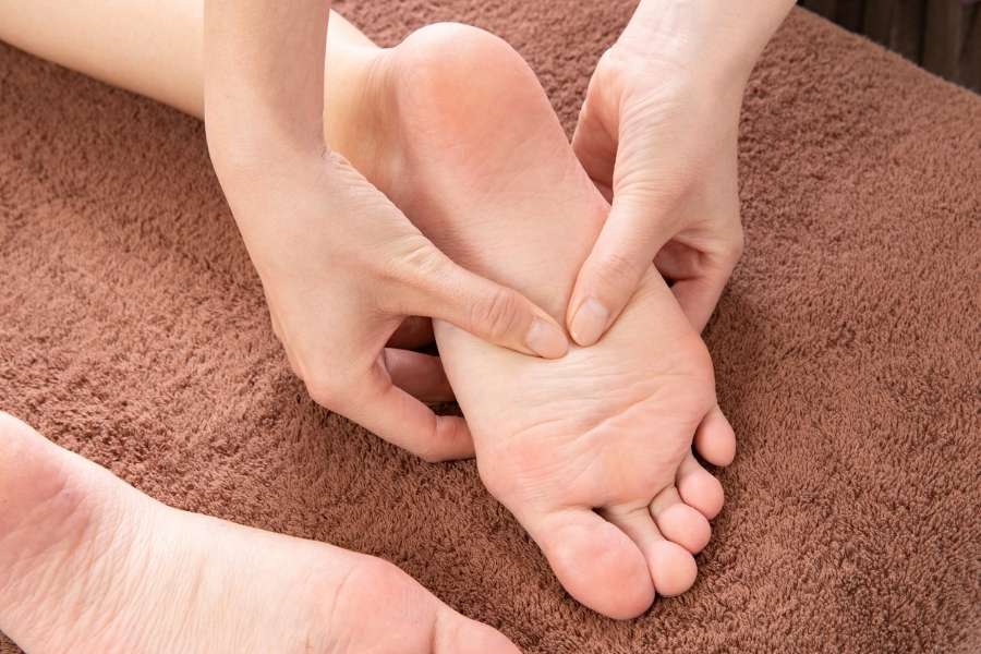Gros plan sur les mains d'un praticien effectuant une pression ciblée sur la voûte plantaire d'un pied lors d'une séance de massage des pieds sur une serviette marron.