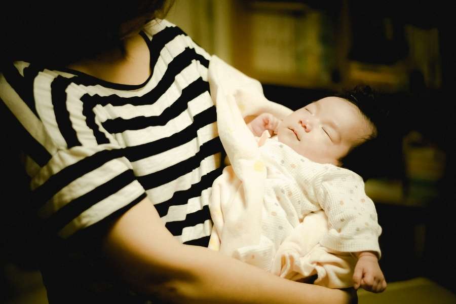 Un bébé nouveau-né dort paisiblement dans les bras de sa maman qui porte un t-shirt à rayures.
