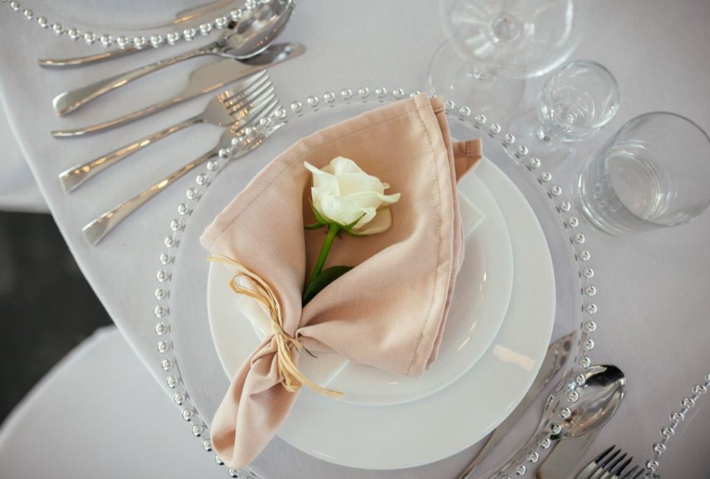 Assiette blanche surmontée d'une serviette beige et d'une rose blanche illustrant des idées décoration mariage minimaliste et épurée.