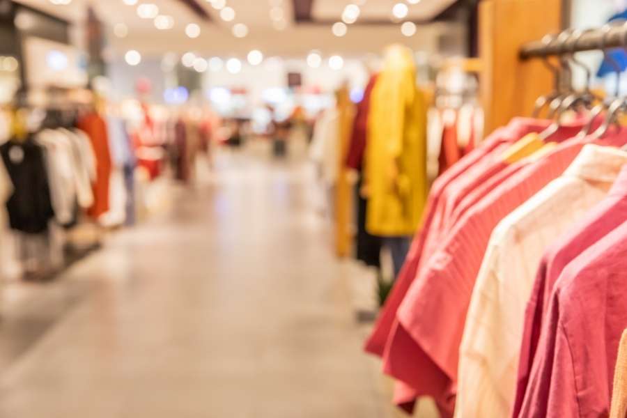 Portants remplis de vêtements roses et colorés soigneusement alignés dans l'allée d'une boutique de mode.